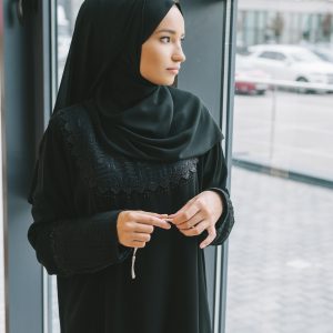 thoughtful young muslim woman with prayer beads looking at window